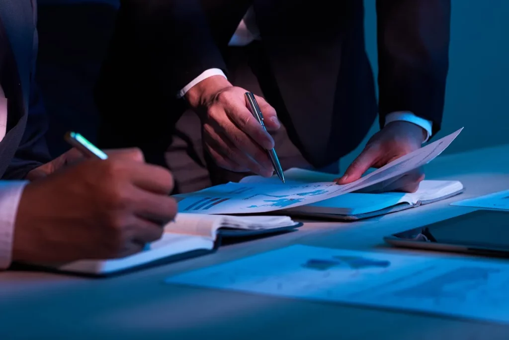 Duas pessoas em uma reunião analisando documentos e gráficos financeiros em um ambiente de trabalho iluminado, simbolizando valuation corporativo.