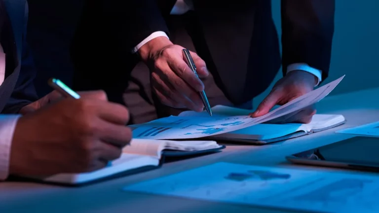Duas pessoas em uma reunião analisando documentos e gráficos financeiros em um ambiente de trabalho iluminado, simbolizando valuation corporativo.