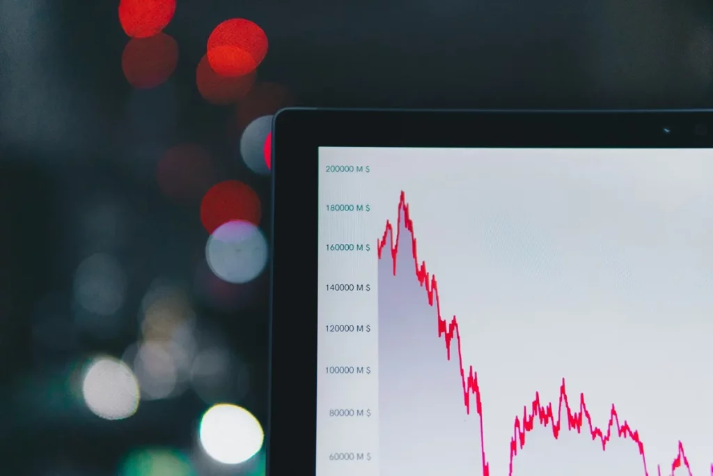 Tela exibindo gráfico financeiro com linha de queda em vermelho, simbolizando volatilidade de mercado, com fundo desfocado.