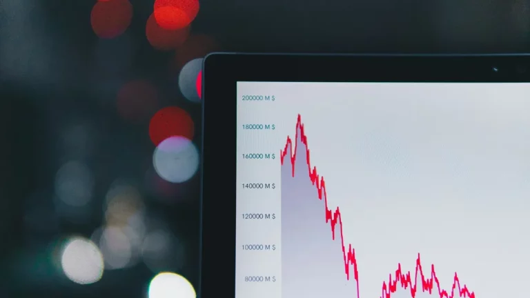 Tela exibindo gráfico financeiro com linha de queda em vermelho, simbolizando volatilidade de mercado, com fundo desfocado.