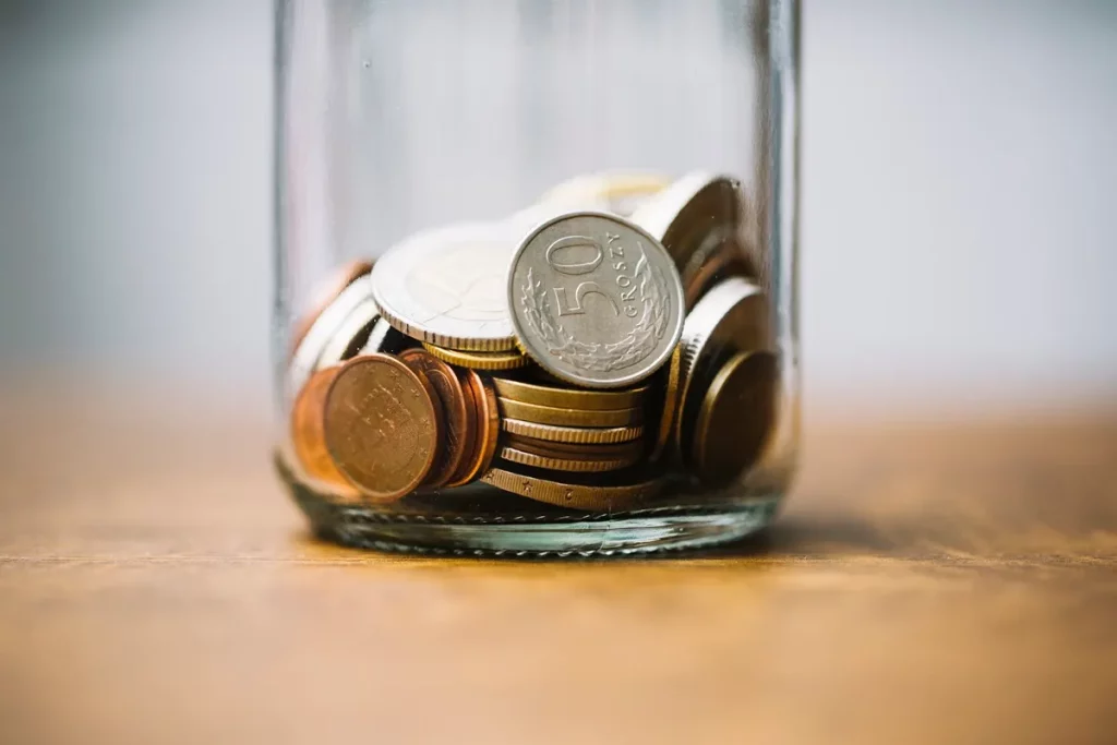 Um pote de vidro contendo moedas de diferentes tamanhos e valores, representando poupança e gestão financeira.