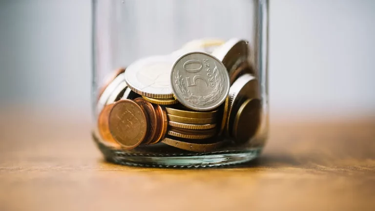 Um pote de vidro contendo moedas de diferentes tamanhos e valores, representando poupança e gestão financeira.