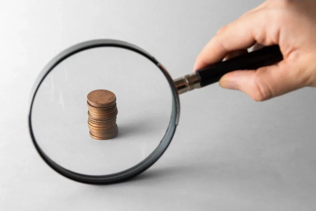 Uma lupa ampliando uma pilha de moedas, simbolizando a análise detalhada de finanças e investimentos
