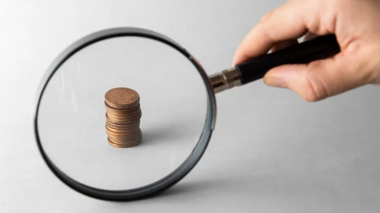 Uma lupa ampliando uma pilha de moedas, simbolizando a análise detalhada de finanças e investimentos