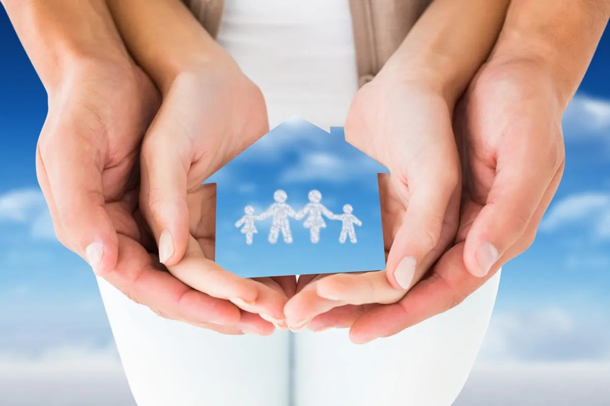 Mãos segurando uma figura em forma de casa com uma família representada no centro, simbolizando proteção e segurança familiar