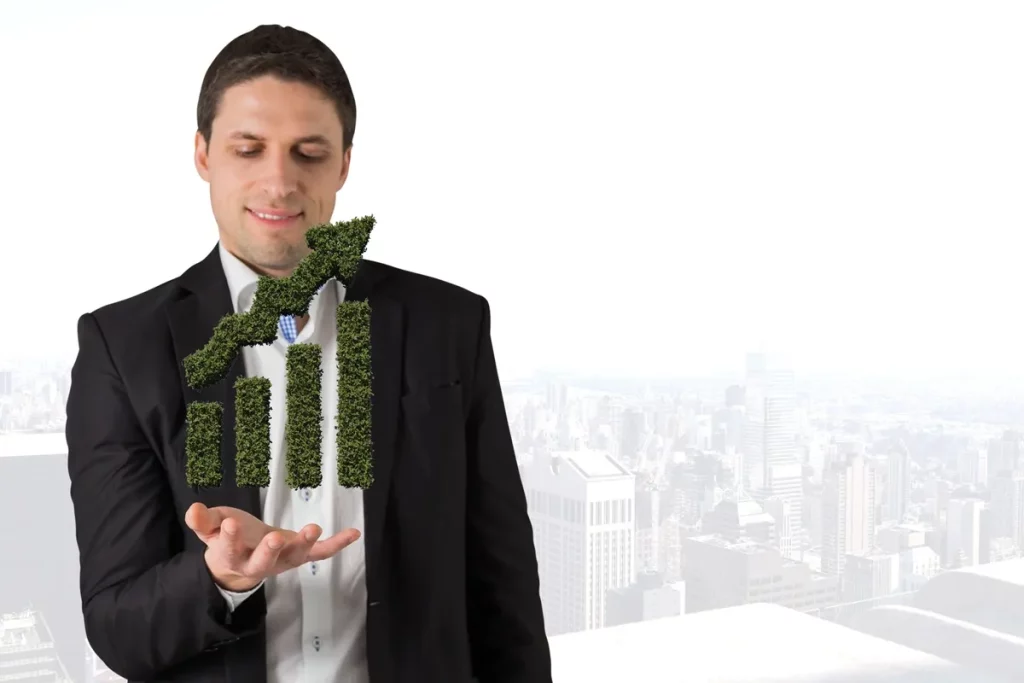 Homem de terno preto e camisa branca segura um gráfico de barras verde feito de vegetação, simbolizando crescimento sustentável e economia verde. O fundo mostra uma cidade com prédios altos e atmosfera esbranquiçada, destacando a relação entre desenvolvimento econômico e práticas ambientais responsáveis.