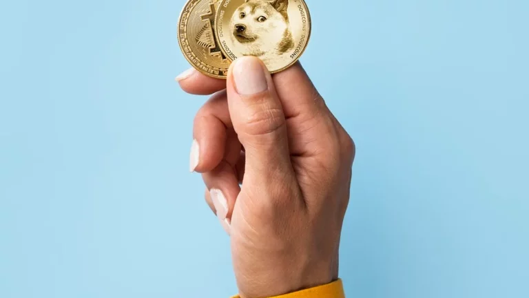 Pessoa segurando duas moedas físicas representando criptomoedas, incluindo a Dogecoin, com fundo azul claro.