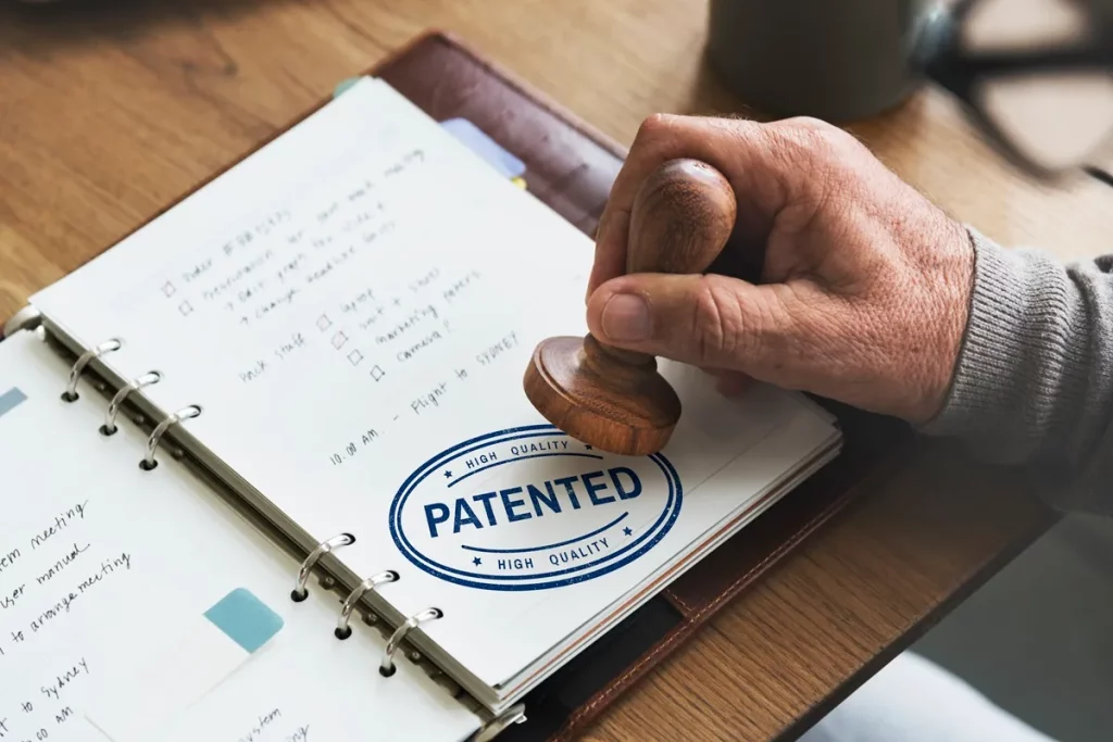 Pessoa carimba a palavra "PATENTED" em caderno de anotações, simbolizando o registro de uma patente