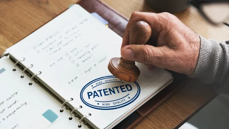 Pessoa carimba a palavra "PATENTED" em caderno de anotações, simbolizando o registro de uma patente