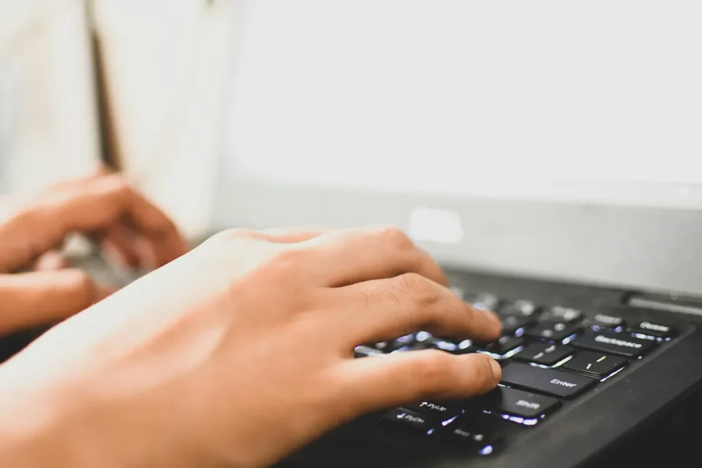 Mãos digitando em teclado de notebook, representando atividades profissionais ou cálculo de hora trabalhada.