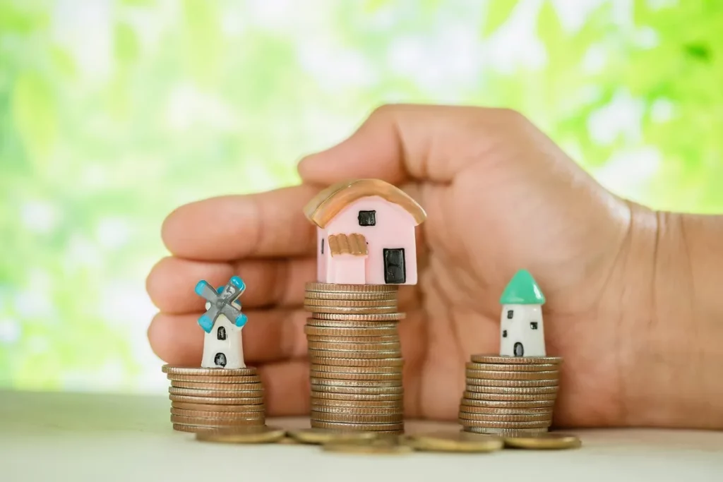 Casas em miniatura sobre pilhas de moedas representando herança, patrimônio e planejamento financeiro familiar.