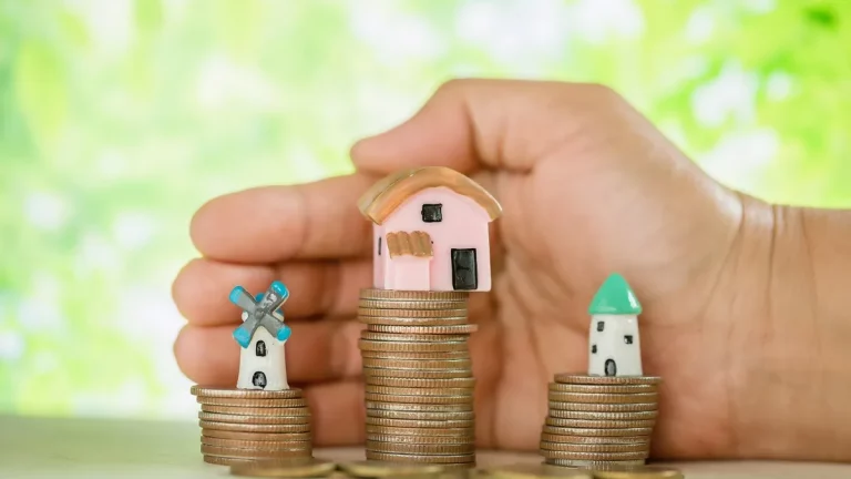Casas em miniatura sobre pilhas de moedas representando herança, patrimônio e planejamento financeiro familiar.