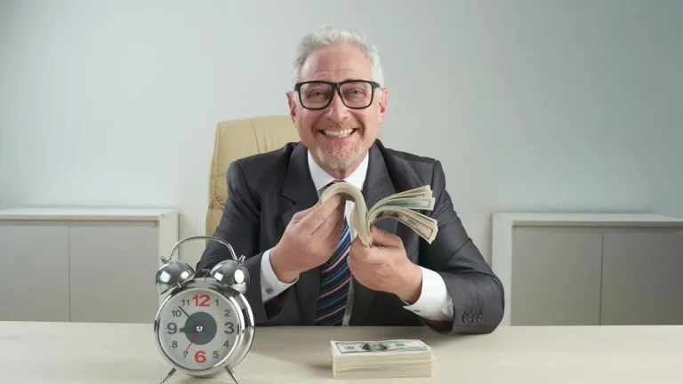 Homem sorridente de terno contando maços de dinheiro sentado à mesa, com despertador metálico ao lado, simbolizando rendimento financeiro ao longo do tempo.