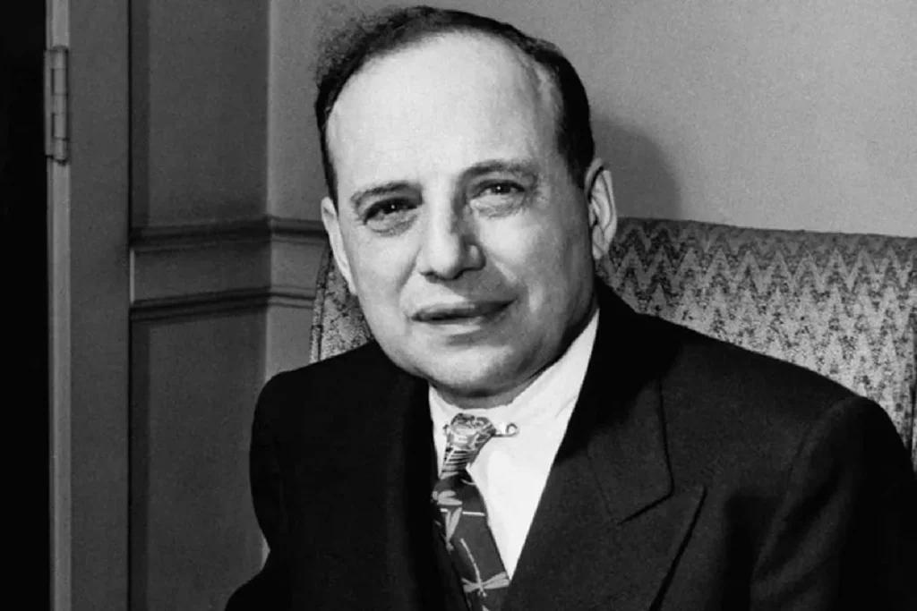 Retrato em preto e branco de Benjamin Graham, vestindo terno e gravata, sentado em poltrona com expressão serena.