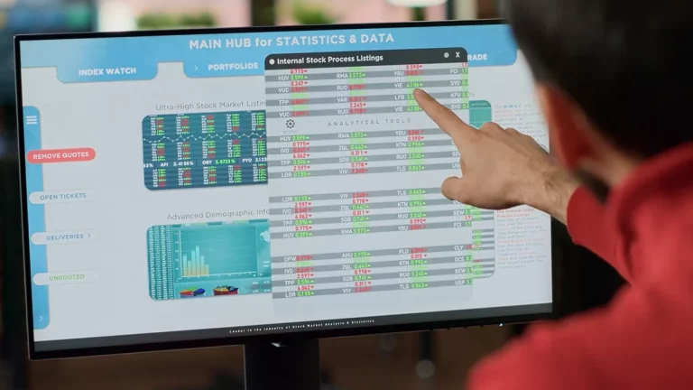 Homem apontando para tela de computador com tabelas, gráficos e dados de ações, analisando cotações em sistema de estatísticas financeiras.