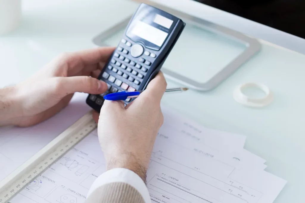 Imagem de um homem usando uma calculadora e uma caneta, preenchendo um formulário DARF sobre uma mesa com documentos fiscais