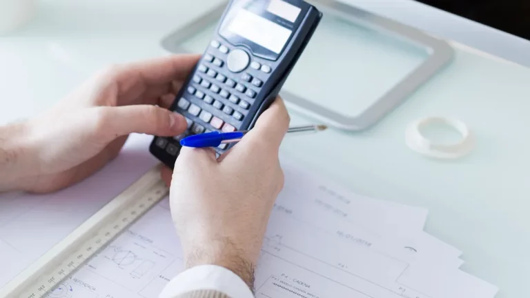 Imagem de um homem usando uma calculadora e uma caneta, preenchendo um formulário DARF sobre uma mesa com documentos fiscais