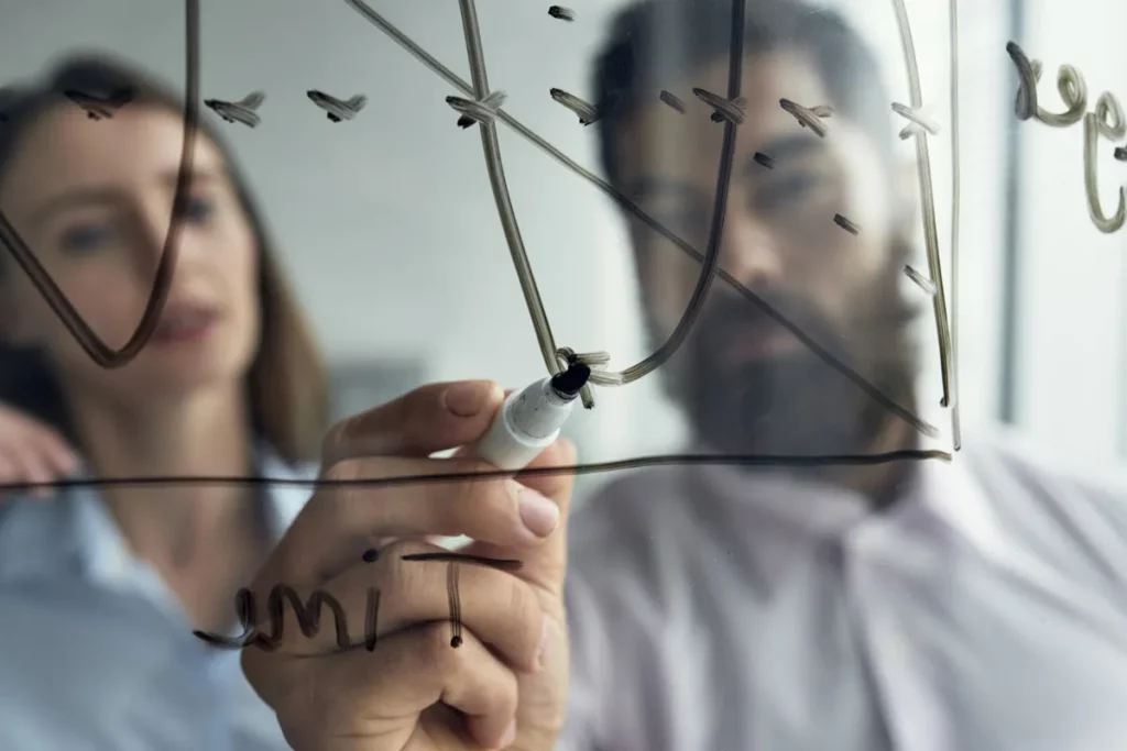 Dois profissionais analisando gráfico desenhado em vidro