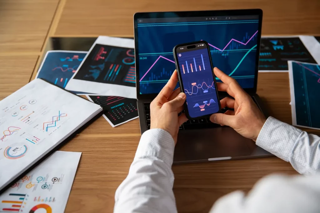 Pessoa analisando gráficos financeiros em notebook e celular