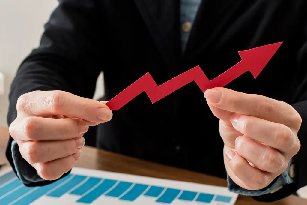Pessoa segurando seta vermelha representando crescimento em gráfico, com barras azuis ao fundo