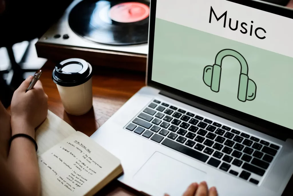 Pessoa estudando sobre música com notebook, caderno e toca-discos ao fundo.