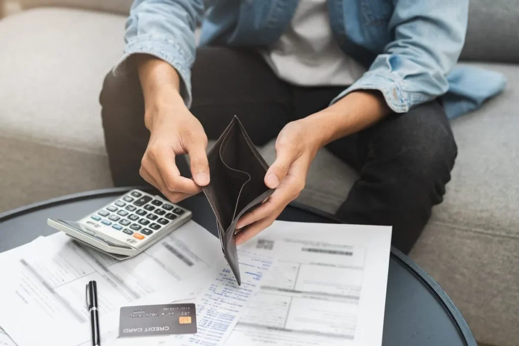 Pessoa segurando uma carteira vazia, com calculadora, cartões e contas em uma mesa, representando dificuldades financeiras e o uso do cheque especial.