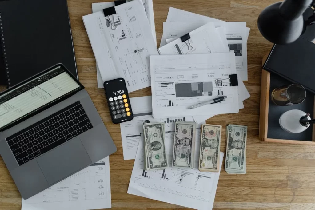Mesa de trabalho com laptop, calculadora, documentos financeiros e notas de dólar, representando como investir em dólares e planejamento financeiro.