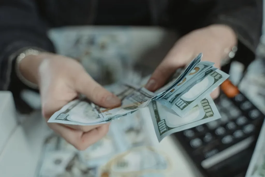 Mãos contando notas de dólar americano, com calculadora ao fundo, representando como investir em dólares na B3.