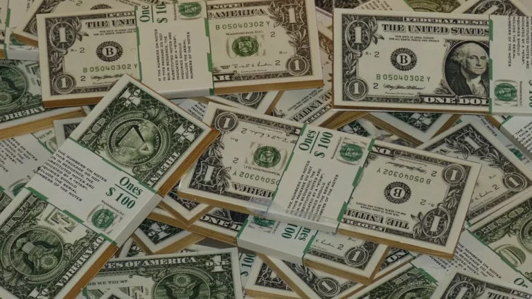 Pilhas e notas soltas de dólares americanos, com destaque para cédulas de $1 e maços de $100, simbolizando como investir em dólares.