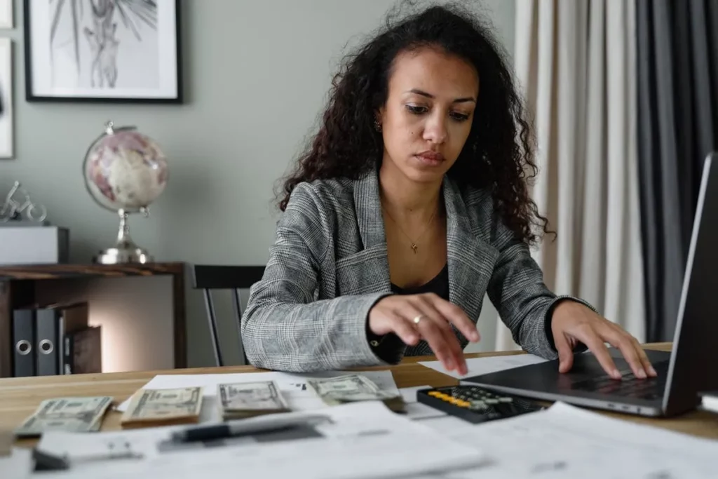 Mãos segurando um smartphone com calculadora e um caderno com anotações, com notas de Euro e moedas em primeiro plano, representando o planejamento financeiro e como investir para iniciantes.