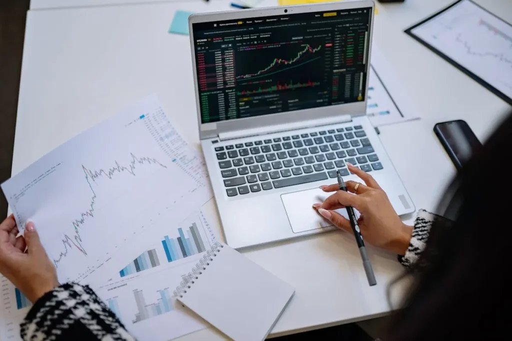 "Pessoa analisando gráficos de investimentos em notebook e documentos impressos, buscando qual é a melhor corretora para investir."