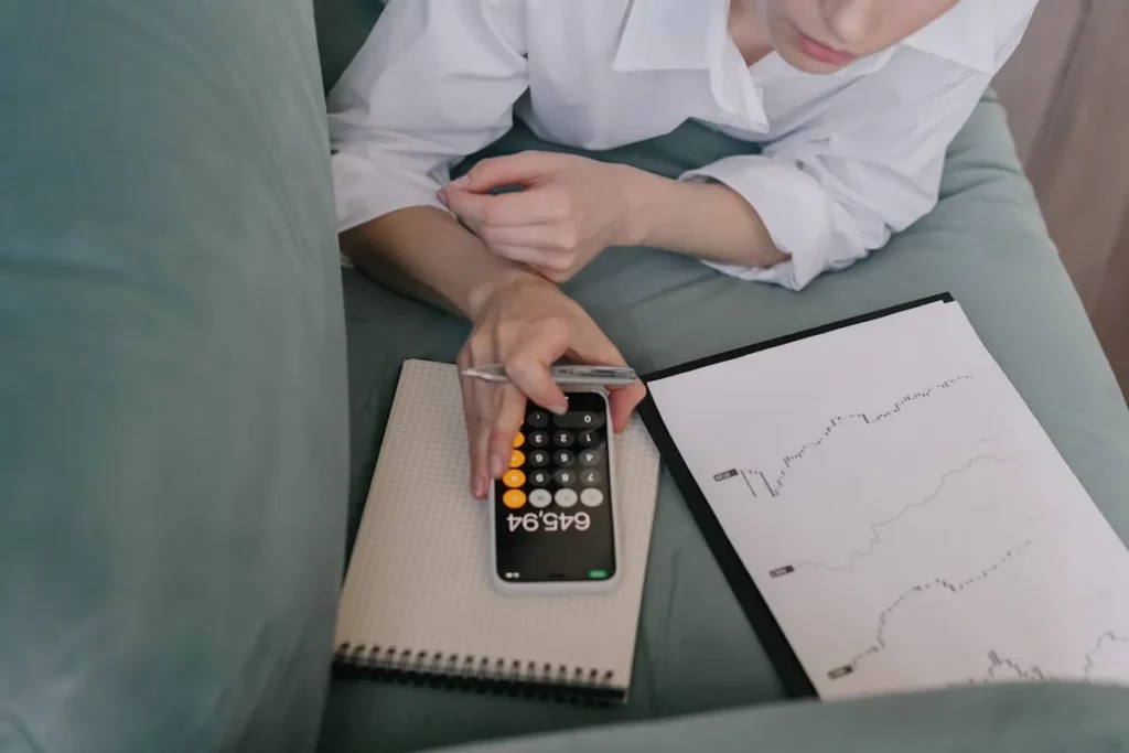 Pessoa usando calculadora e analisando gráficos financeiros, buscando qual é a melhor corretora para investir.