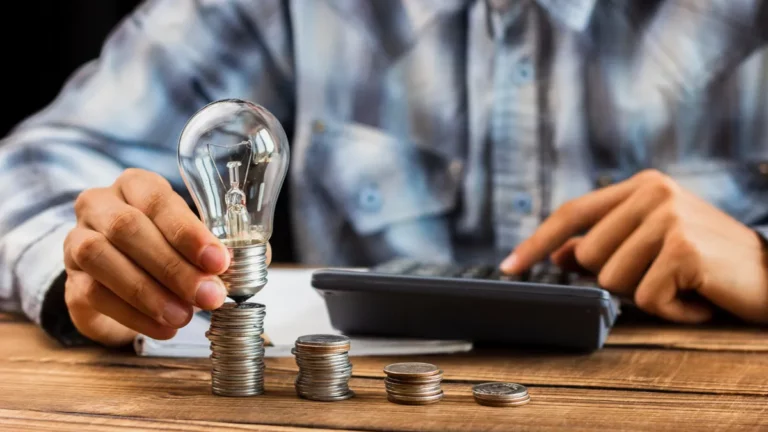 Pessoa segurando lâmpada sobre pilhas de moedas e usando calculadora, simbolizando ideias e planejamento para saber qual é a melhor forma de investir dinheiro.