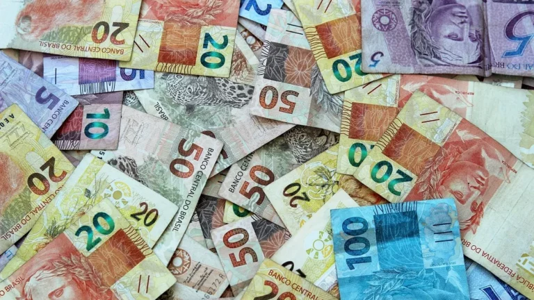 Fundo com diversas notas de reais (R5,R20, R50,R100) espalhadas, representando o capital inicial e os possíveis retornos de um investimento de 1.000 reais.