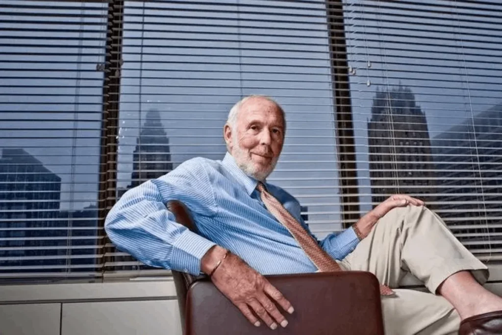 Retrato de Jim Simons, fundador da Renaissance Technologies, sorrindo e sentado em uma poltrona em frente a uma janela com persianas e vista para a cidade.