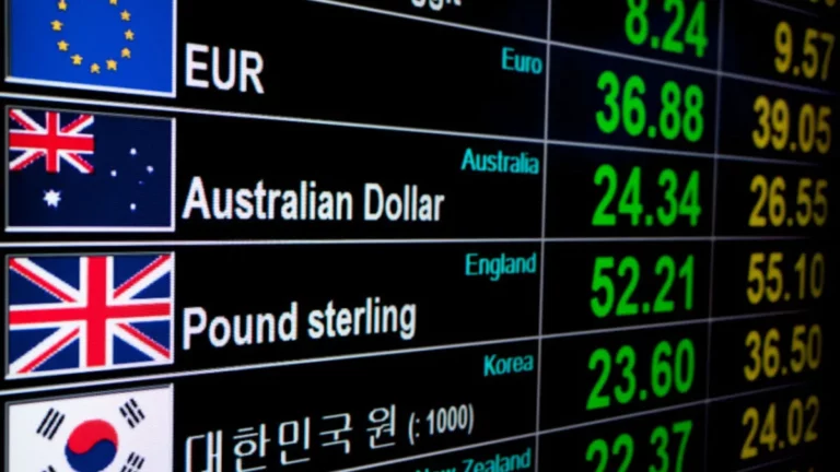 Uma exibição digital mostra taxas de câmbio de várias moedas globais, incluindo Euro, Dólar Australiano, Libra Esterlina e Won Sul-Coreano, com suas respectivas bandeiras e valores numéricos em verde e laranja.