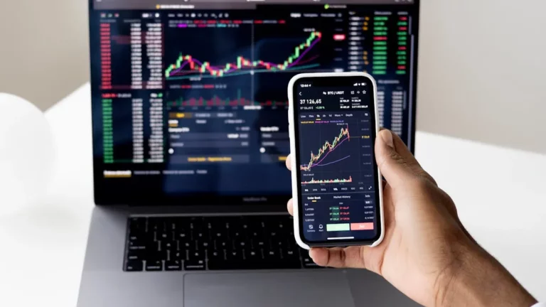 Pessoa usando o celular e o computador para analisar gráficos