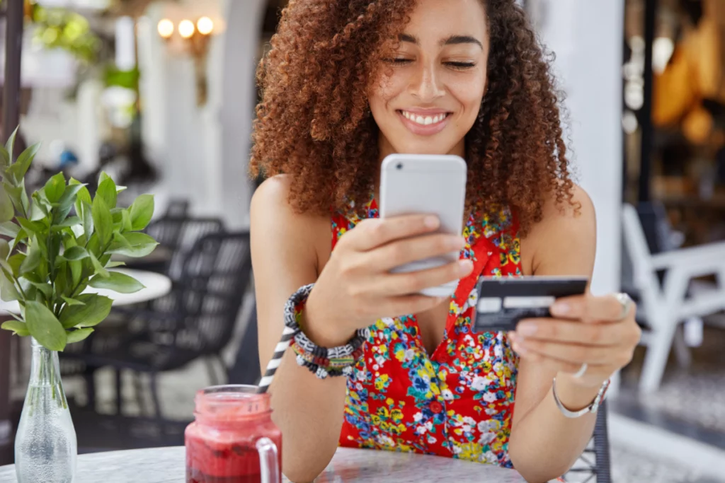 Mulher usando o celular e segurando cartão de crédito