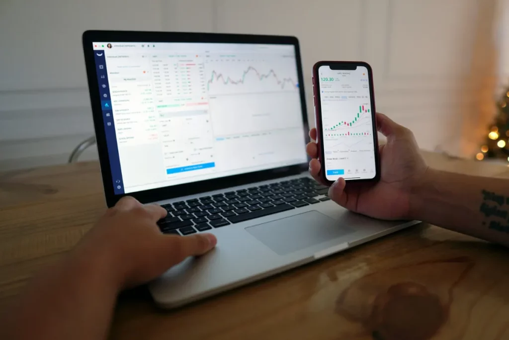 Pessoa analisando investimentos no laptop e celular
