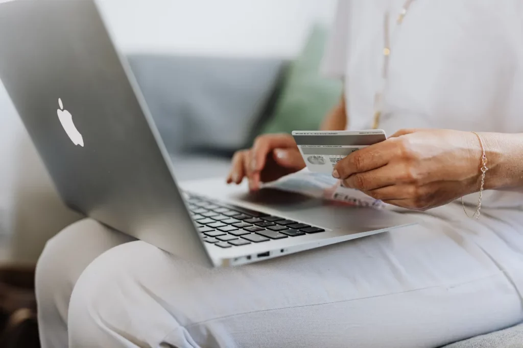 Pessoa utilizando notebook enquanto segura um cartão de crédito com a outra mão.