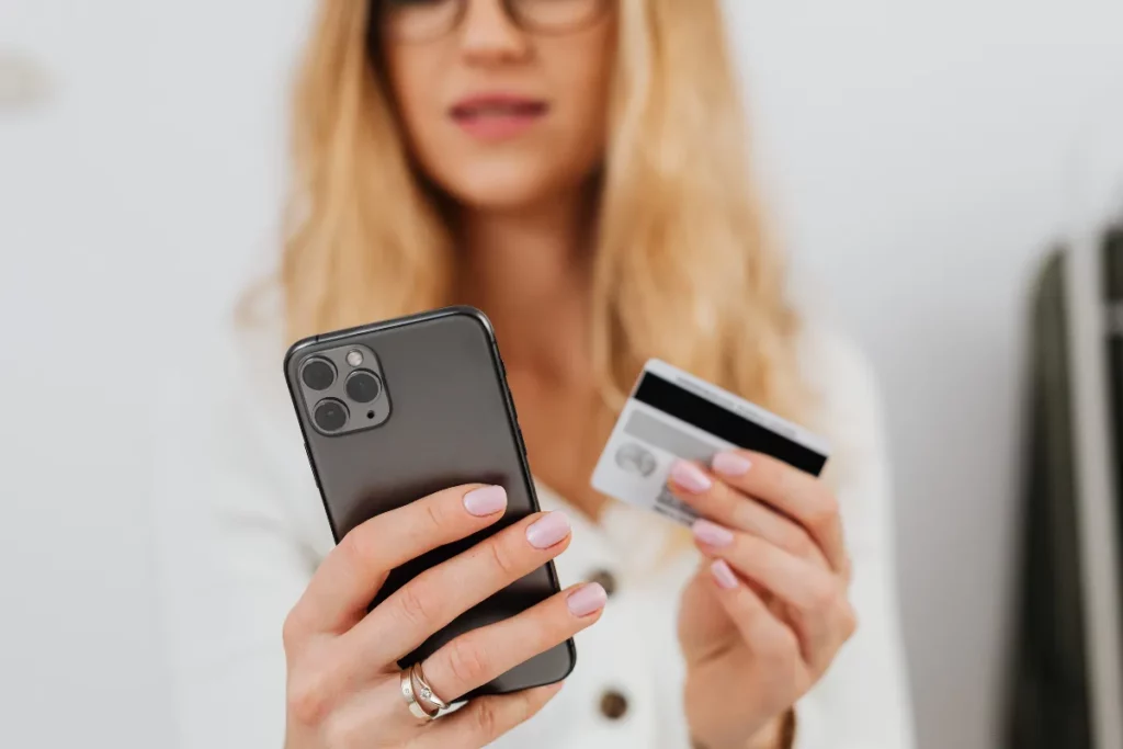 Mulher segurando um celular em uma mão e um cartão de crédito na outra.