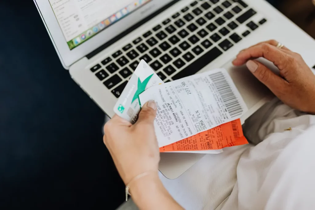 Pessoa utilizando notebook enquanto segura um cartão de crédito e faz anotações em papel.