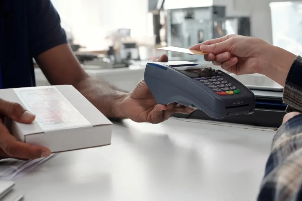 Cliente entregando cartão para pagamento em maquininha enquanto atendente registra a compra.