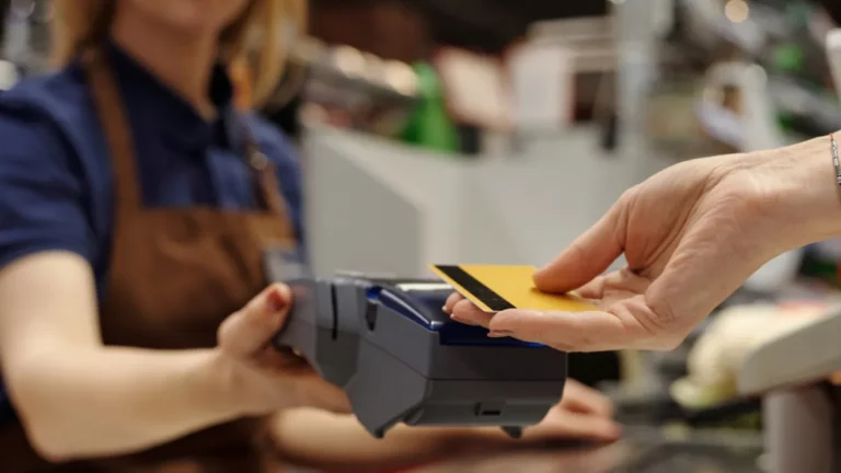 Cliente entregando cartão para pagamento em maquininha enquanto atendente segura o terminal.