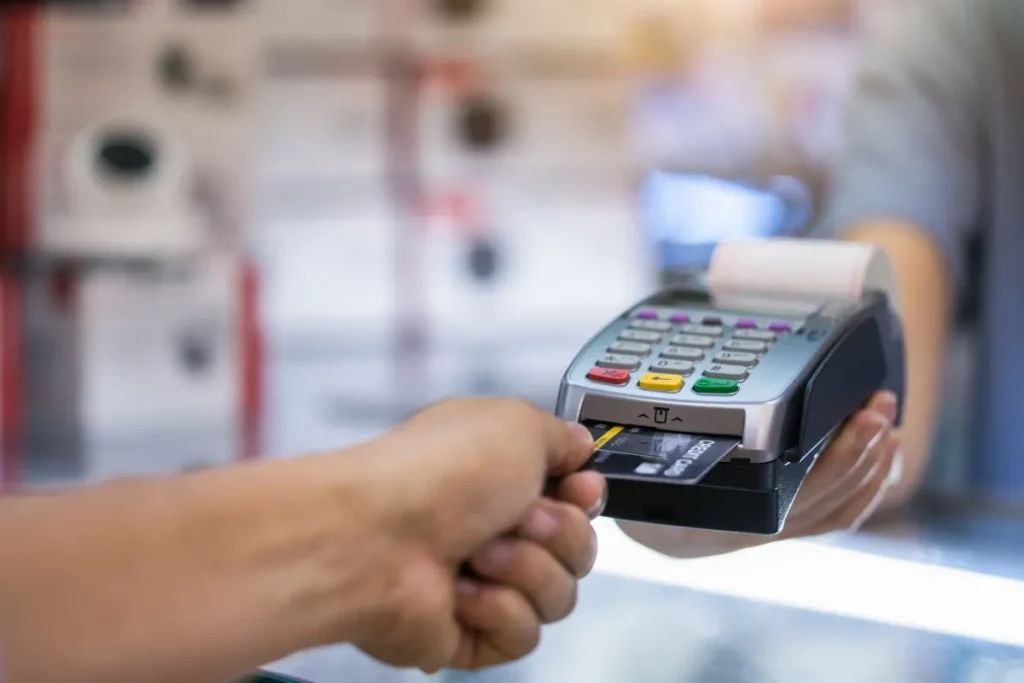 Pessoa aproximando cartão de crédito de uma maquininha de pagamento para realizar compra.