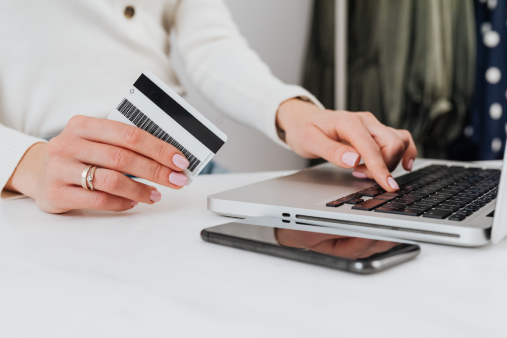 Pessoa segurando um cartão bancário enquanto utiliza um notebook para fazer pagamento online.