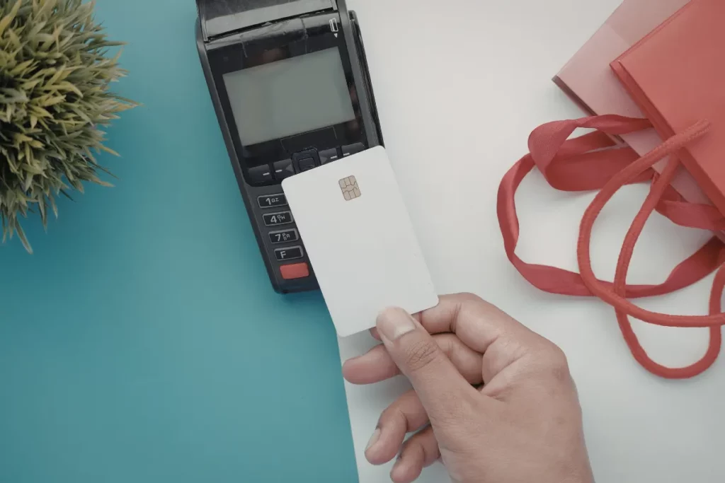 mão aproximando cartão de crédito de uma máquina de pagamento em cima de uma mesa